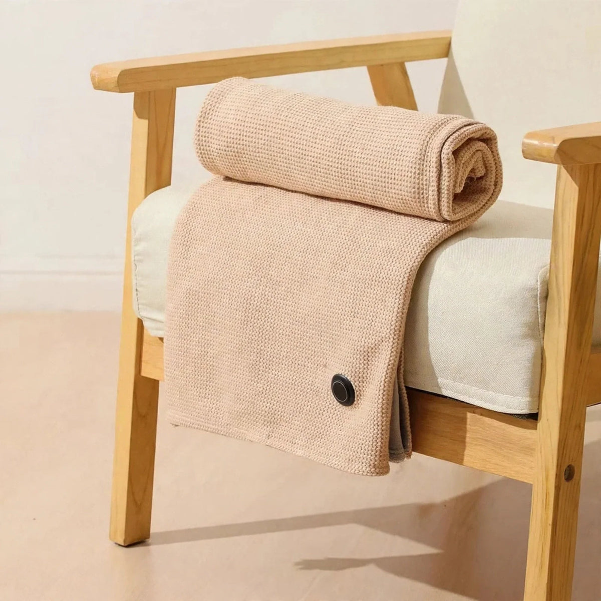 Apricot waffle knit heated shawl with a black control button, rolled and draped over a wooden armchair