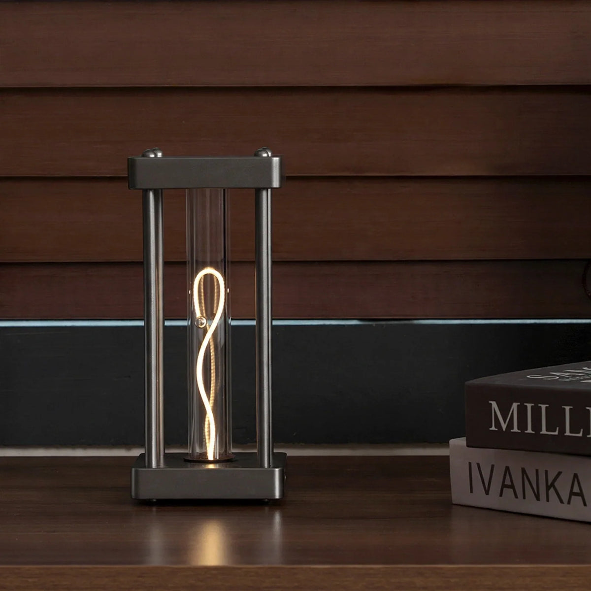 Square metal frame table lamp with a glowing filament tube and a balancing sphere inside.