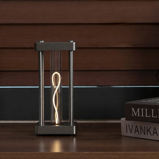 Square metal frame table lamp with a glowing filament tube and a balancing sphere inside.