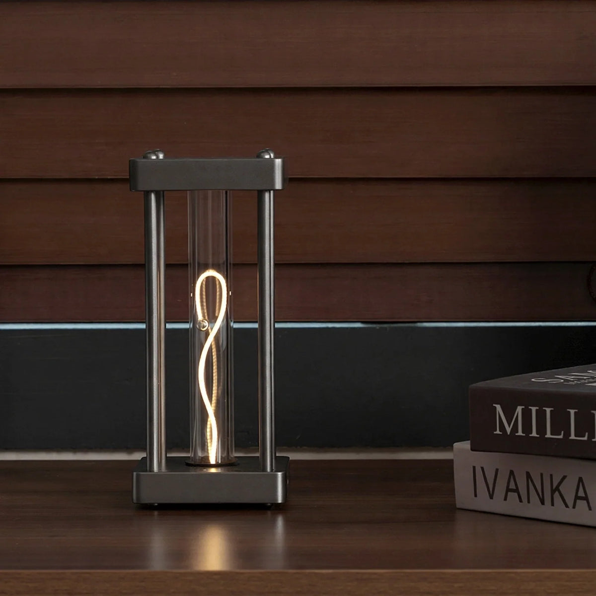 Square metal frame table lamp with a glowing filament tube and a balancing sphere inside.