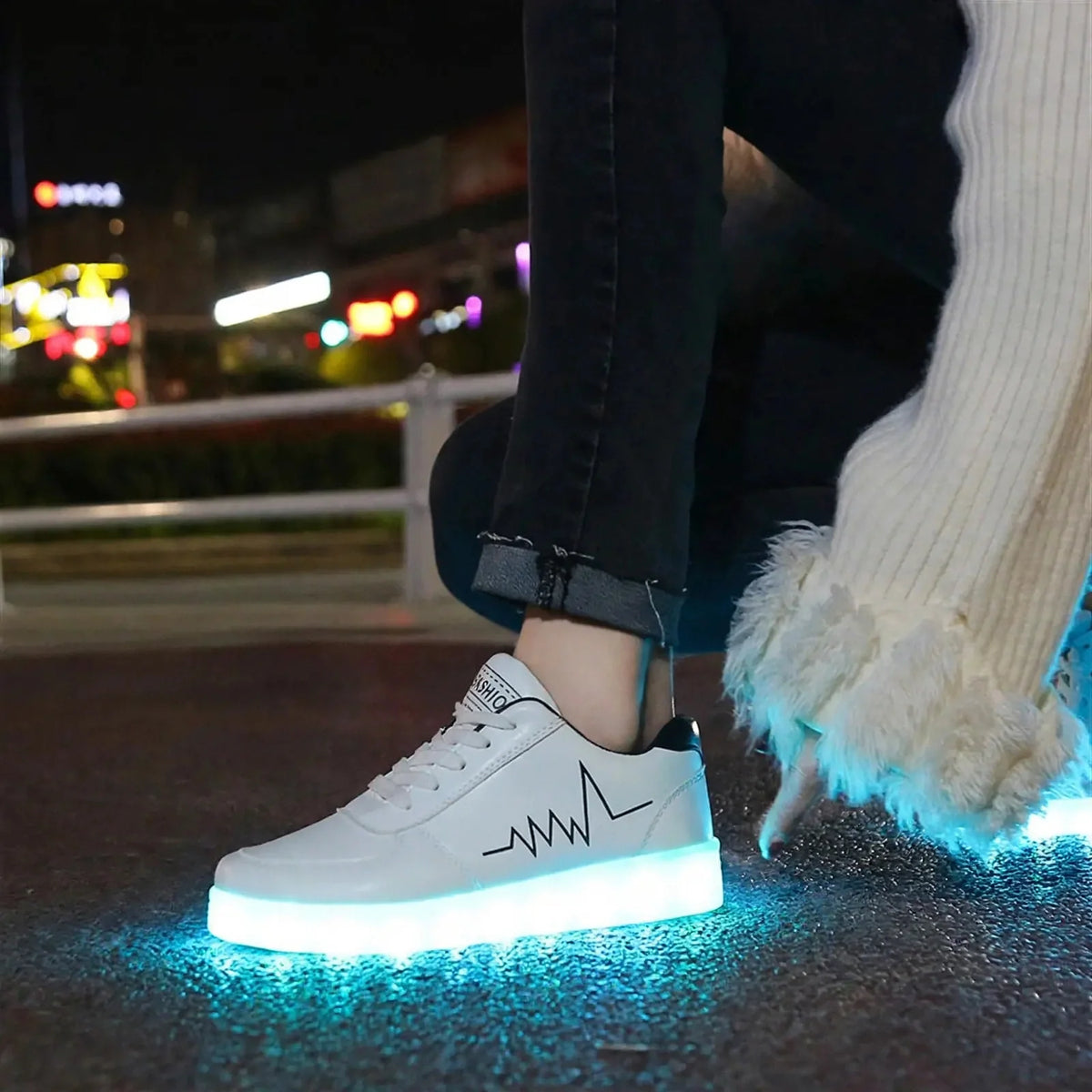 White sneakers with glowing blue soles and a black side heartbeat graphic worn outdoors at night