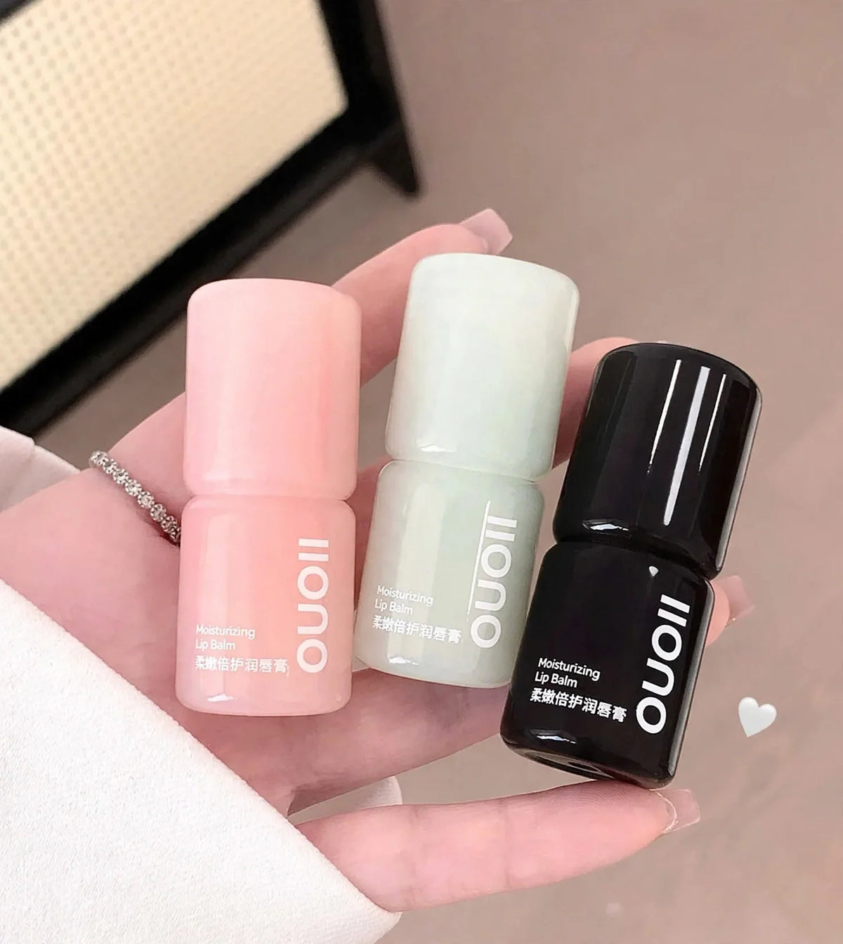 A hand holding three small lip balm containers in pink, light green, and black.