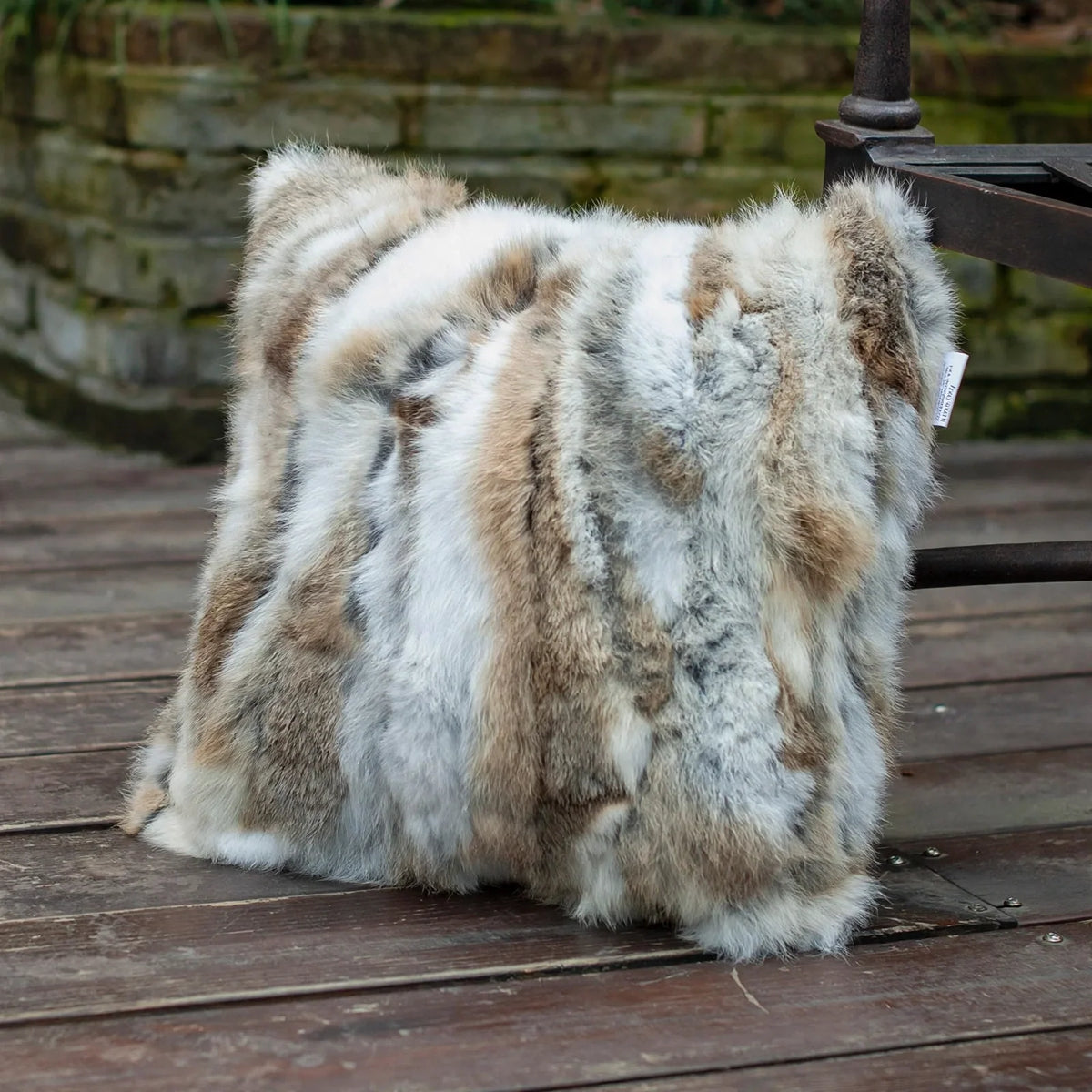 Square patchwork fur pillow cover with a mix of white, brown, and grey tones resting on a wooden deck.