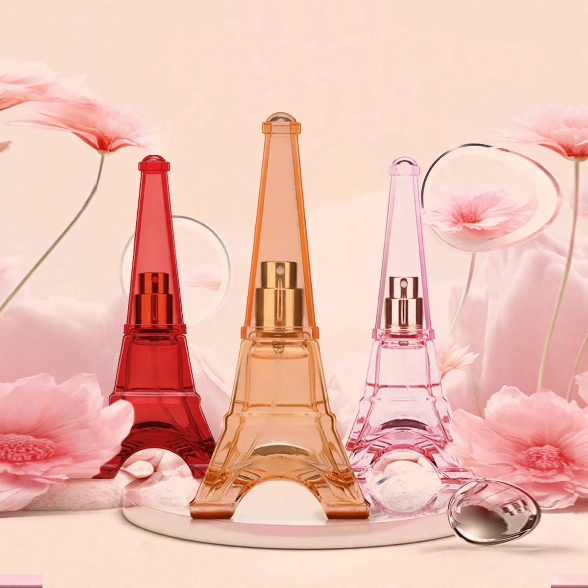 Three Eiffel tower shaped perfume bottles in red, orange, and pink against a pink floral background.