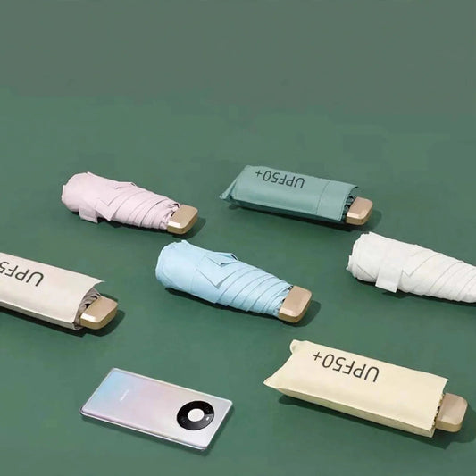 Six compact folded umbrellas in various pastel colors alongside a smartphone on a green surface.