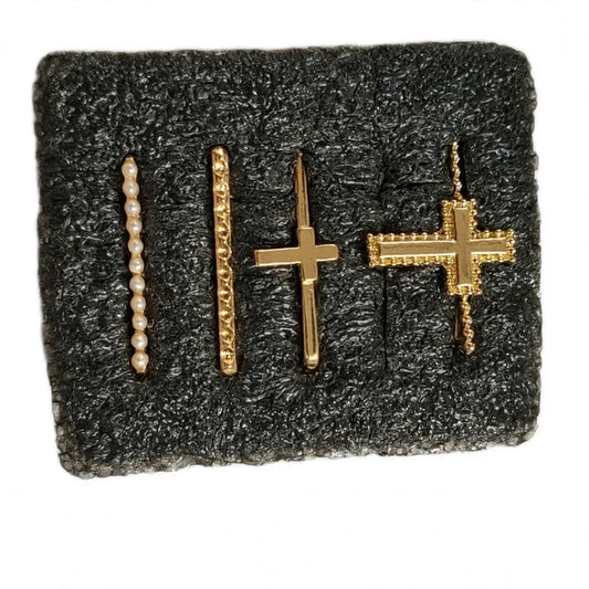 Four gold smartwatch band charms on dark foam, including a pearl bar, textured bar, and two cross designs.