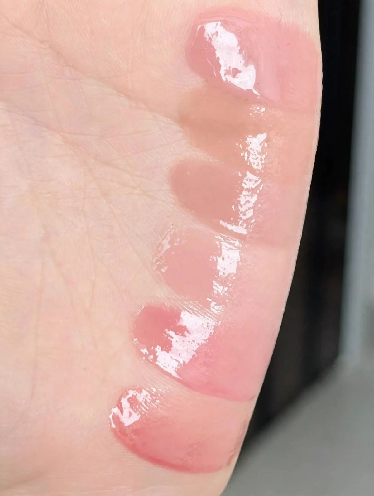 five glossy lip lacquer swatches in pink and nude shades on skin