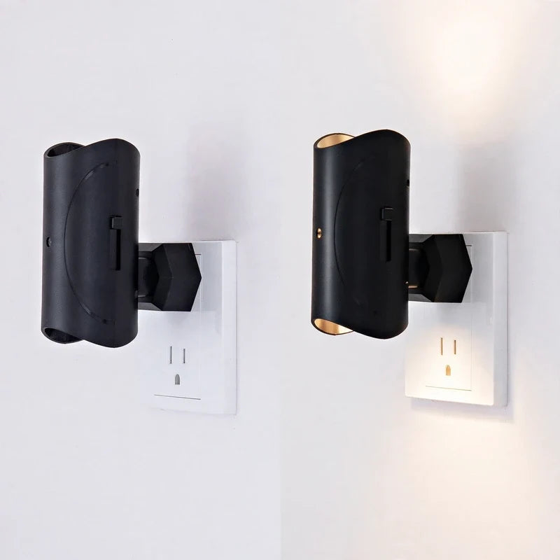 Two black plug-in cylinder night lights plugged into white wall outlets, one unlit and one illuminated.