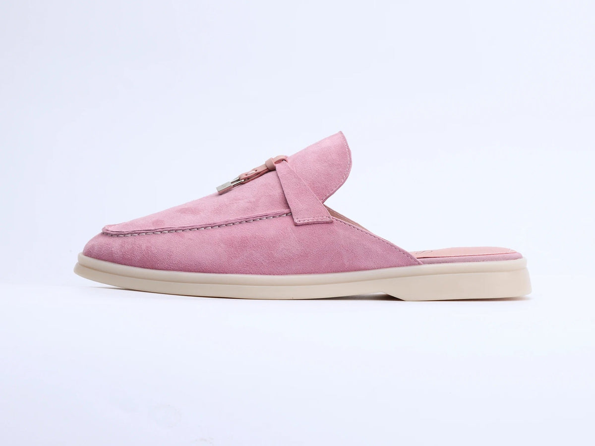 Pink suede mule with a flat sole, tassel, and metal ring detail viewed from the side.