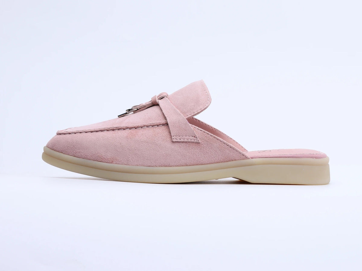 Side view of a pink suede mule with a tassel and metal ring on the upper, set against a plain background.