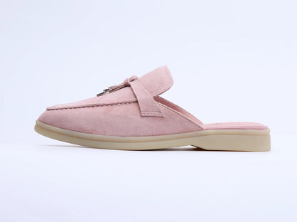 Side view of a pink suede mule with a tassel and metal ring on the upper, set against a plain background.