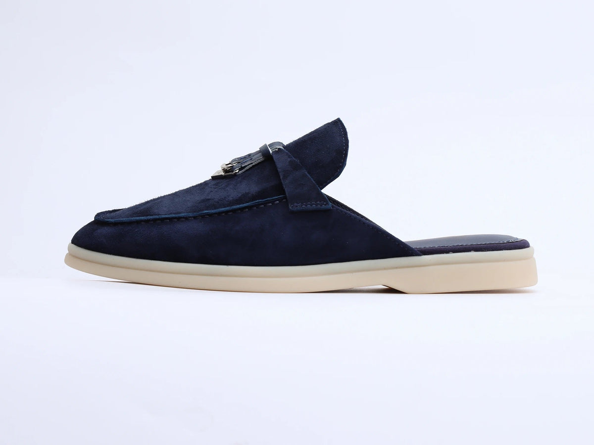 Navy blue suede mule with side strap and tassel detail on a light sole, side profile