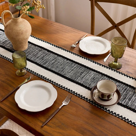 Woven black and white table runner on wooden dining table with place setting