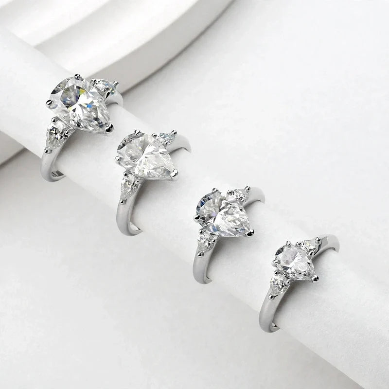 Four silver engagement rings with pear-cut center stones displayed in a row on a white surface.