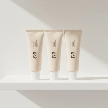 Three identical pale beige moisture cream tubes with white caps standing upright on a white shelf.