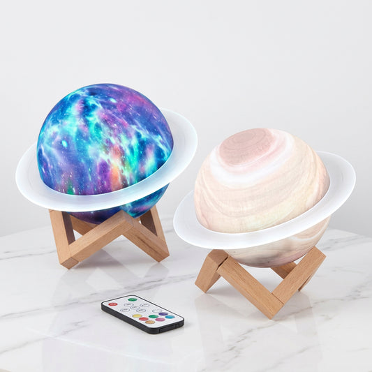 Two Saturn planet night light lamps with wooden stands and a remote control on a surface.