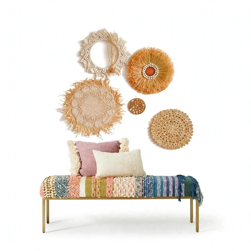 Multicolor woven bench with pillows beneath a wall arrangement of round textured art pieces.