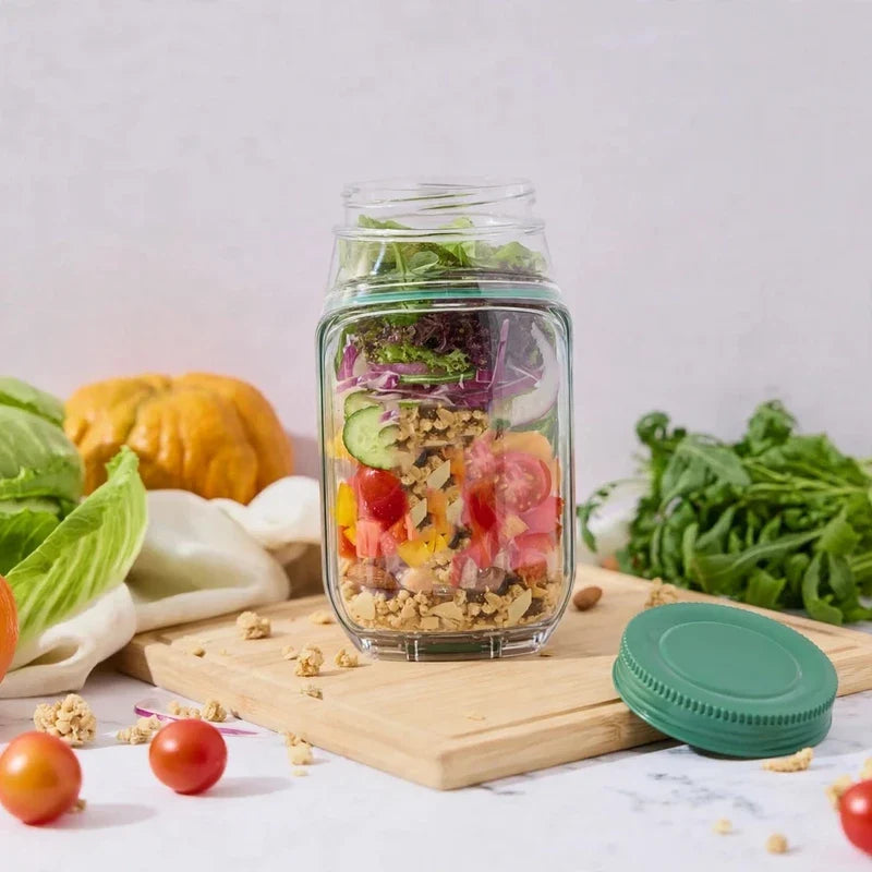 Clear vertical salad container cup filled with layers of vegetables and greens, with a green lid on a wooden cutting board