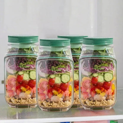 Four clear plastic jars with green lids filled with layered salad ingredients on a white shelf.