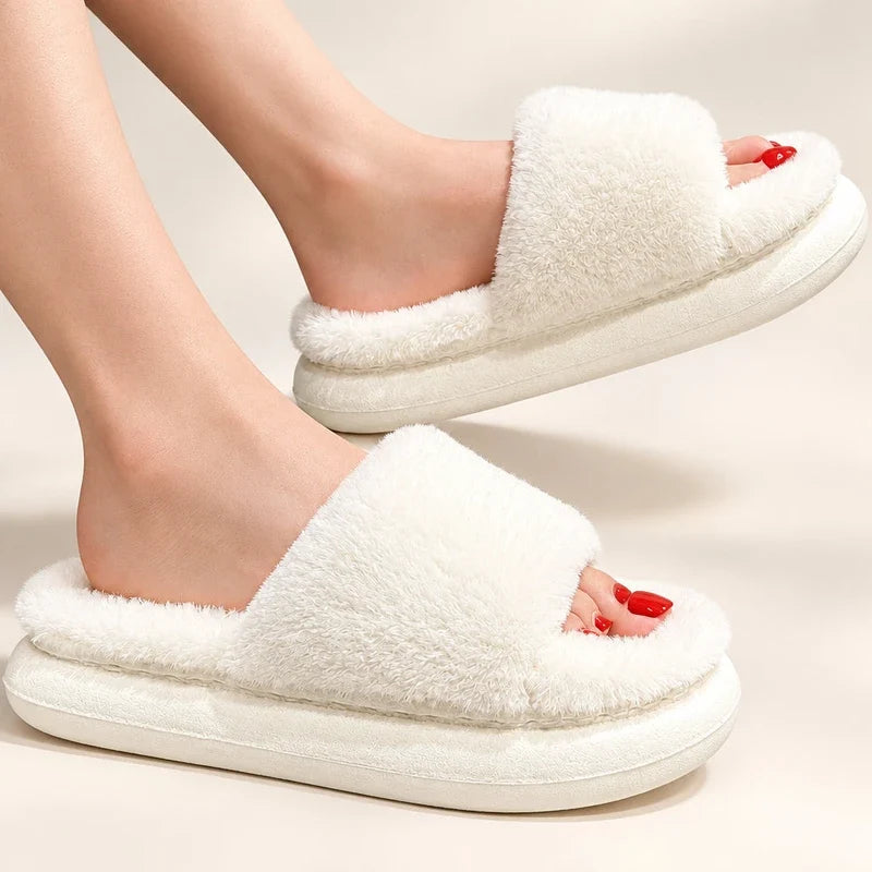 White fuzzy open-toe slide slippers with thick cushioned platforms worn on feet.