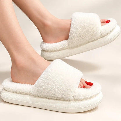 White fuzzy open-toe slide slippers with thick cushioned platforms worn on feet.