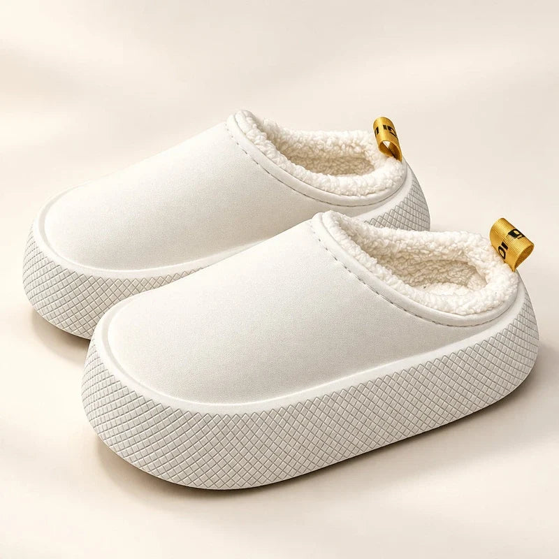 White fleece-lined slip-on slippers with thick textured platform soles and small yellow heel pull tabs.