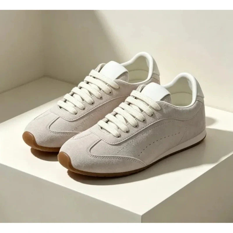 Pair of off-white suede low-top sneakers with white laces and gum rubber soles on a white surface.