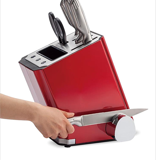 Red knife block holding stainless steel knives and shears, showing a hand sharpening a blade on the side slot.