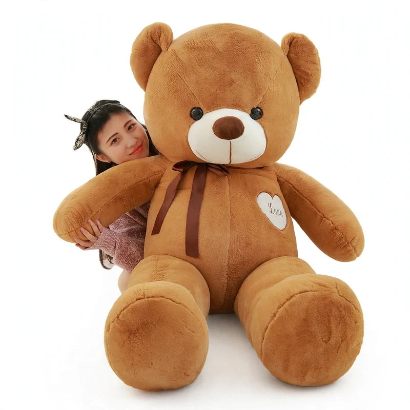 Giant brown plush teddy bear with a brown bow and heart patch, being hugged by a woman from behind