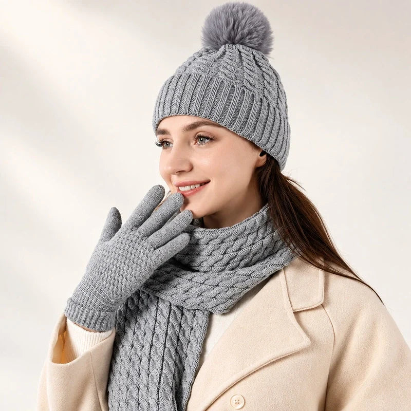 Woman wearing a gray cable-knit beanie with pom-pom, matching scarf, and gloves.