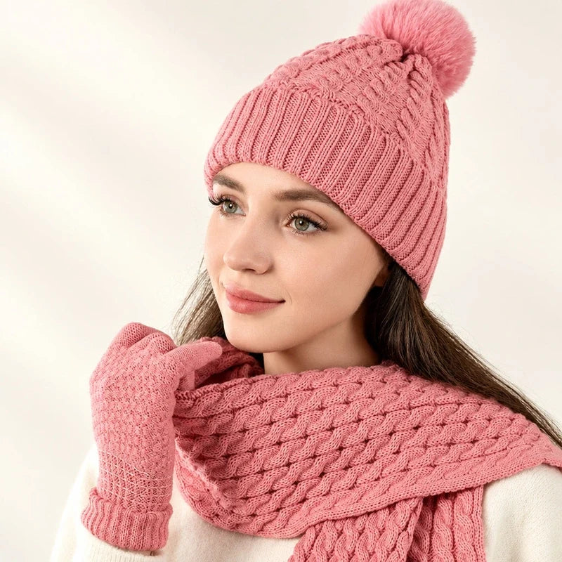 A woman wearing a pink cable-knit pom-pom beanie, scarf, and matching gloves.