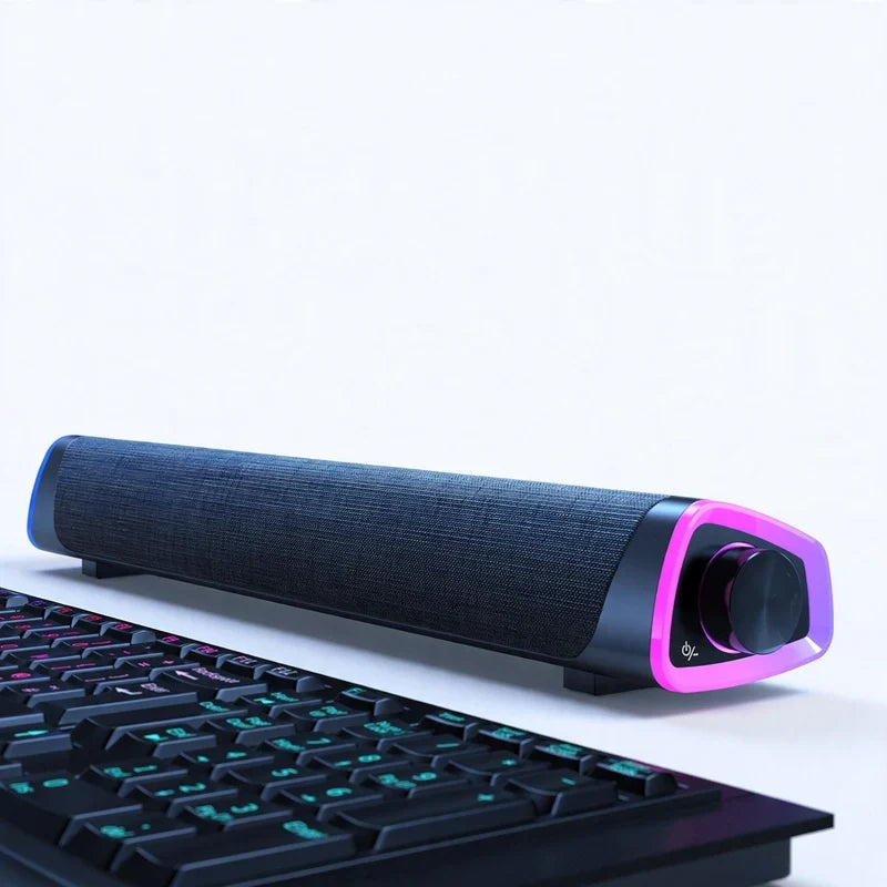 Black wireless soundbar with fabric mesh and pink illuminated side panel, positioned above a keyboard.