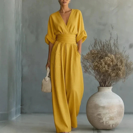 Woman wearing a yellow V-neck jumpsuit with wide legs and cuffed sleeves, holding a small woven bag.