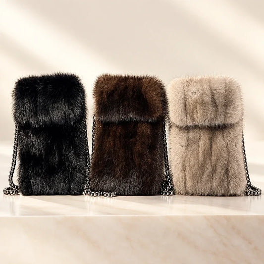 Three furry crossbody bags in black, brown, and beige with chain straps on a surface.