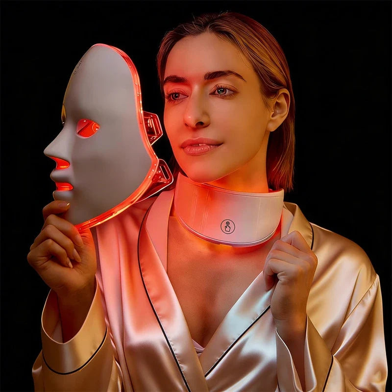 Woman in satin robe holding a glowing red light therapy face mask, wearing a matching neck panel.