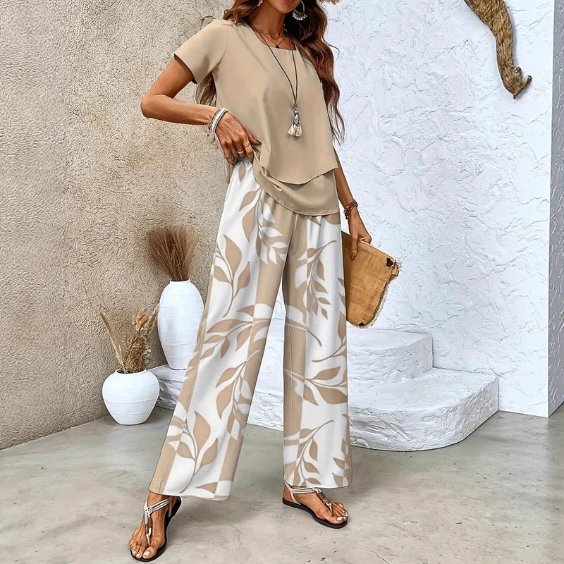 Woman wearing beige short-sleeve top and white pants with beige leaf print, holding a clutch.
