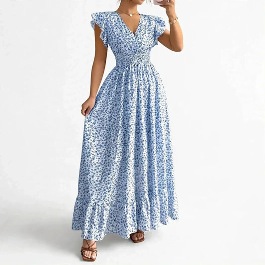A woman wearing a blue and white floral maxi dress with ruffled sleeves and a smocked waist.