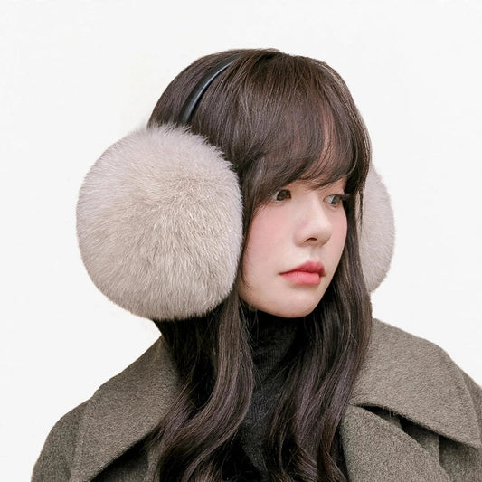 Woman wearing fluffy light gray fur earmuffs and a dark turtleneck.