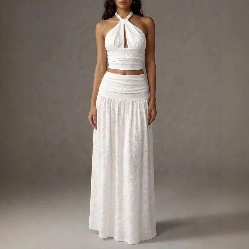 White two-piece set featuring a halter crop top with a keyhole cut and a matching pleated maxi skirt.