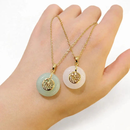 Two round jade pendant necklaces with gold chains and gold symbol accents held in a hand.