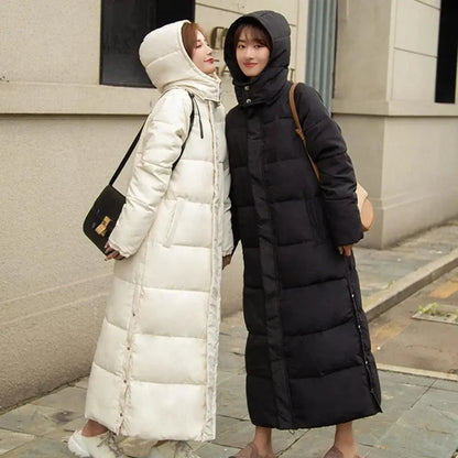 Two women wearing long hooded puffer coats, one white and one black, standing outdoors.