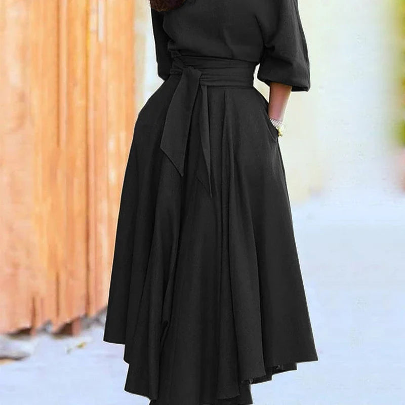Black midi dress with a tied waist belt and pleated skirt, worn outdoors.