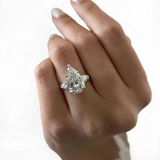 A pear-cut gemstone ring with side stones worn on a hand.