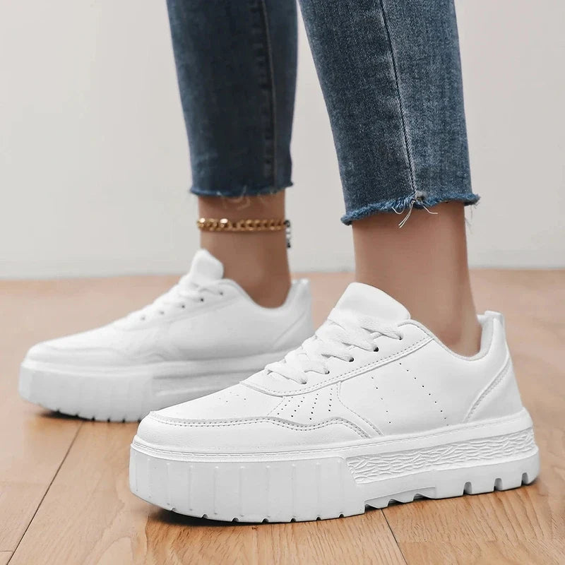 Person wearing white platform sneakers with thick textured soles and blue jeans.