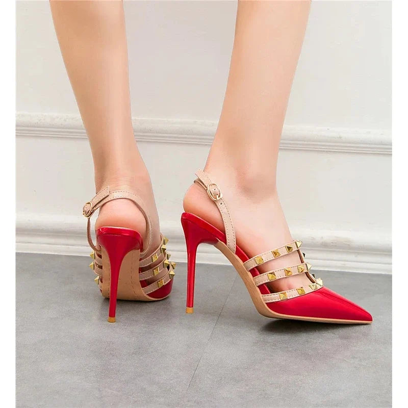 Red pointed-toe stiletto pumps with studded beige straps and slingback buckles worn on feet.