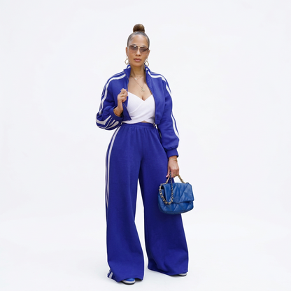 Woman wearing a blue zip-up jacket and wide-leg trousers loungewear set with white side stripes.