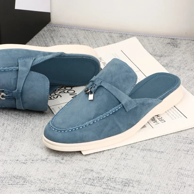 Blue suede flat mules featuring a strap and small padlock detail.