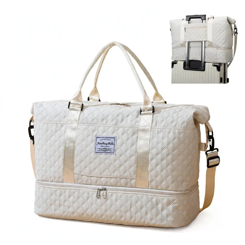 White quilted travel duffel bag with dual top handles, shoulder strap, bottom zip compartment, and luggage sleeve.