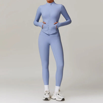 Model wearing a periwinkle blue long-sleeve full-zip activewear jacket and matching leggings with white socks and sneakers.