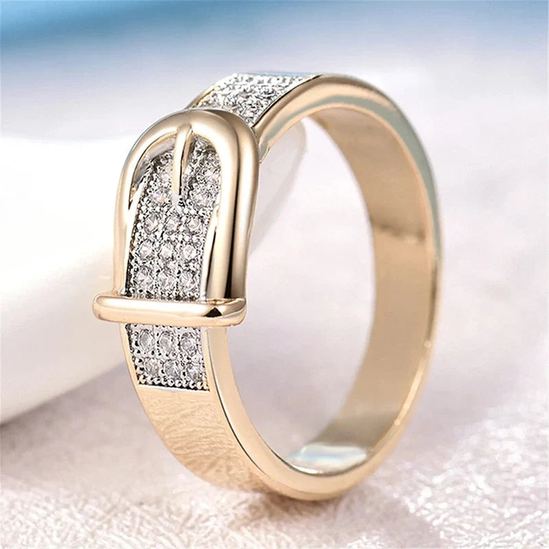 Gold band ring featuring a buckle-shaped accent paved with small cubic zirconia stones.